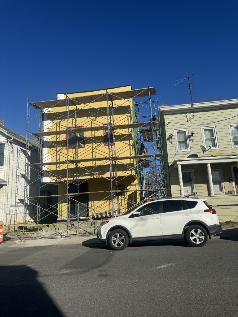 Stucco installation in progress on side of yellow house with scaffolding.