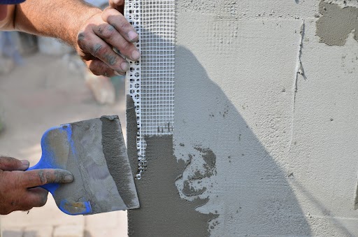 Man applying cement with trowel on wall for stucco installation.